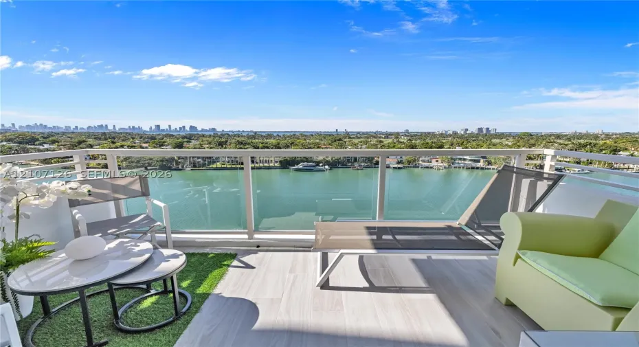 Private balcony featuring tile flooring, artificial turf accents, and a glass-paneled railing with open water and skyline scenery
