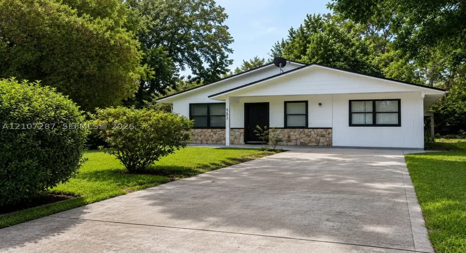 Single-story exterior featuring white horizontal siding, a stone veneer base, a concrete driveway, and mature landscaping