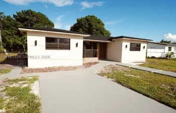Single-story exterior featuring a light-toned stucco facade, a dark-toned flat roof, recessed entryway, and a concrete walkway