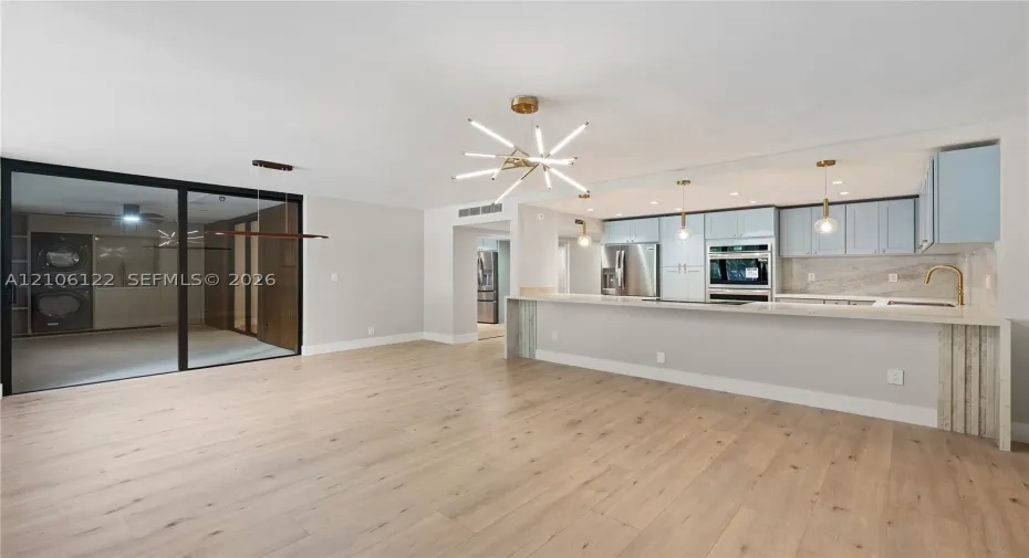 Kitchen featuring custom cabinetry, light-toned stone-finish countertops, stainless steel built-in appliances, a modern multi-arm chandelier, and wide-plank wood-finish flooring