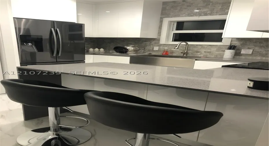 Kitchen featuring high-gloss white cabinetry, quartz countertops, a stainless steel farmhouse sink, and a stone tile backsplash