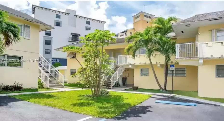 Multi-level exterior featuring light-toned stucco siding, open-air metal staircases, elevated private balconies with metal railings, and a landscaped courtyard