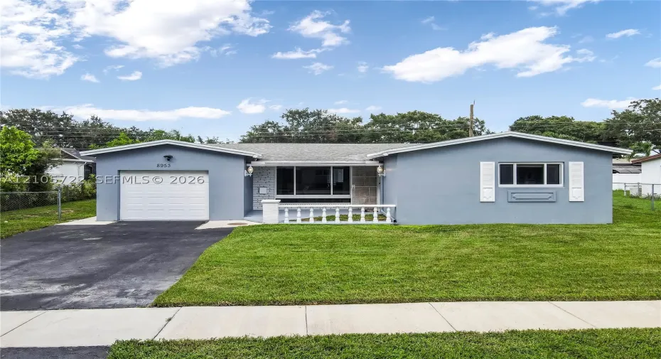 Single-story residence featuring a gray stucco exterior, white louvered shutters, an attached one-car garage, and a decorative white porch railing