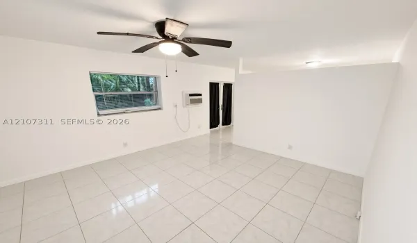 Interior space featuring large-format ceramic tile flooring, a ceiling fan with integrated lighting, a single-hung window, and a wall-mounted air conditioning unit
