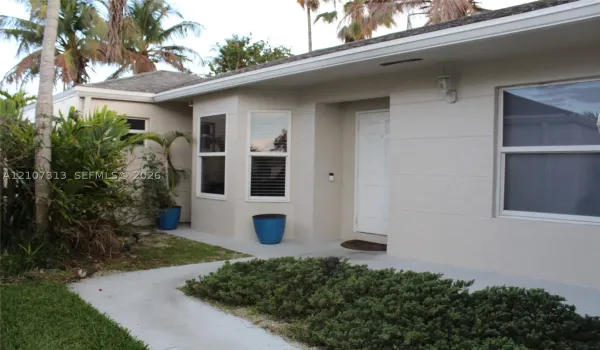 Single-story exterior featuring a smooth stucco facade, bay window, concrete walkway, and integrated wall-mounted lighting