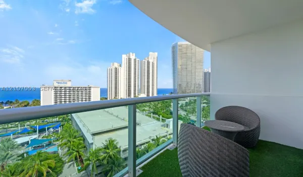 Covered balcony featuring a glass and metal railing, synthetic turf flooring, and horizon ocean and city skyline scenery