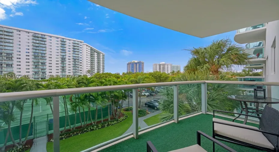 Private balcony featuring a glass-panel railing and green synthetic turf flooring