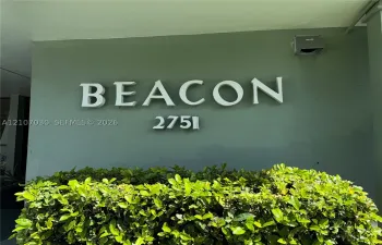 Dimensional building signage featuring raised lettering and address numbers set against a solid-tone exterior wall, accented by a manicured shrub hedge