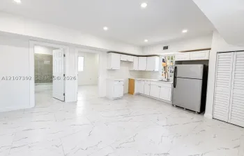 Kitchen area featuring white shaker-style cabinetry, stainless steel refrigerator, stone-patterned tile flooring, recessed ceiling lighting, and louvered closet doors