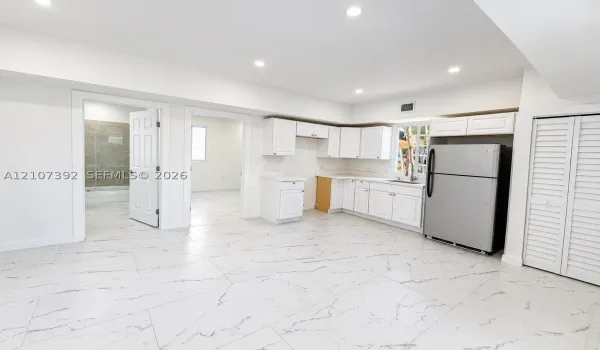 Kitchen area featuring white shaker-style cabinetry, stainless steel refrigerator, stone-patterned tile flooring, recessed ceiling lighting, and louvered closet doors