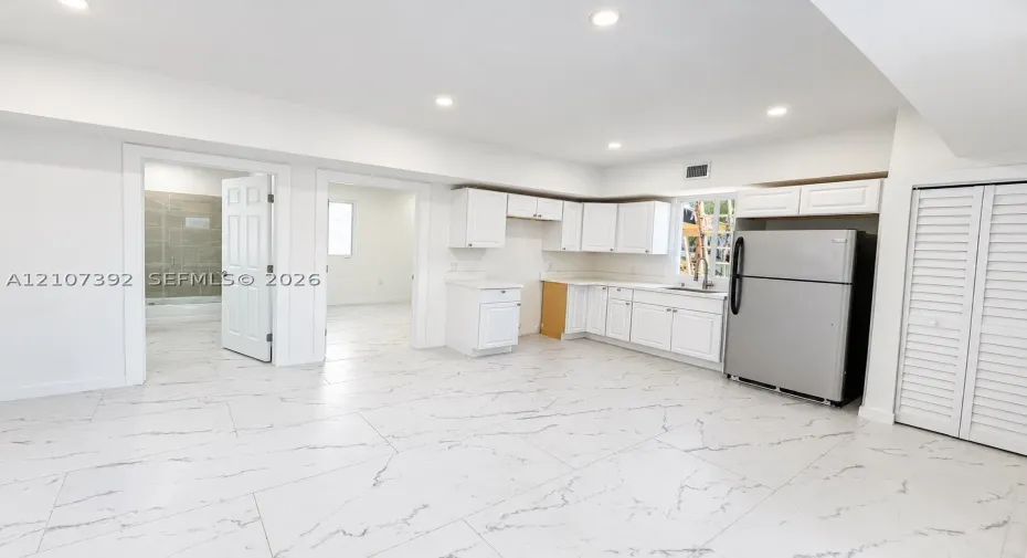Kitchen area featuring white shaker-style cabinetry, stainless steel refrigerator, stone-patterned tile flooring, recessed ceiling lighting, and louvered closet doors