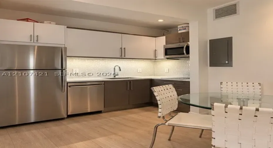 Kitchen featuring stainless steel appliances, two-tone cabinetry, quartz countertops, a textured tile backsplash, and wood-finish flooring