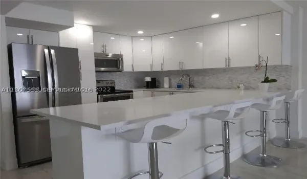 Kitchen featuring white high-gloss cabinetry, stainless steel appliances, quartz countertops, a breakfast bar, and a stone-tile backsplash