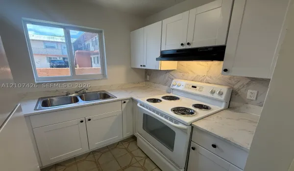 Kitchen featuring white shaker-style cabinetry, patterned stone-finish countertops, herringbone-patterned tile backsplash, stainless steel dual-basin sink, and a white electric range