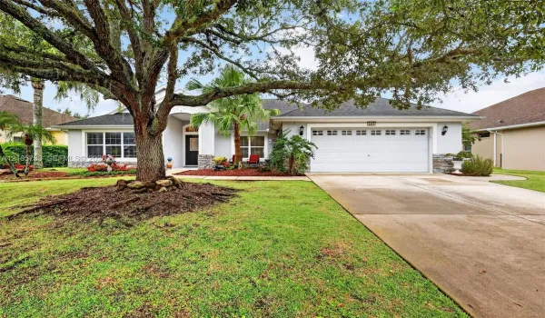 Single-story exterior featuring a two-car garage, stone veneer accents, multi-pane windows, and a mature oak tree in the front lawn