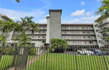 Multi-story exterior featuring a gray stucco facade, tiered balconies with metal railings, and a fenced perimeter