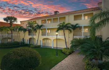 Three-story Mediterranean exterior featuring stucco facade, arched ground-level colonnade, stacked balconies with railings, and terracotta-style roof tiles