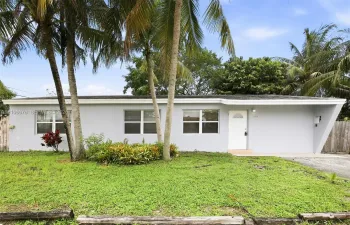 Single-story exterior featuring light-colored stucco siding, a low-slope roofline with a distinctive angled support pillar, and palm-lined landscaping