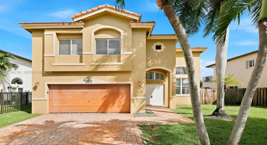 Two-story stucco exterior featuring a tiled roof, arched window detailing, a paved driveway, and a covered entryway