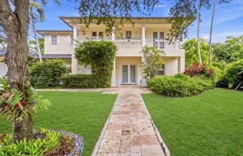 Two-story residence featuring a classic covered front porch, second-level balcony with white railings, stone-paver walkway, and manicured landscaping