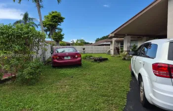 Exterior of the property featuring a covered porch, white vertical-slat fencing, mature palm trees, and manicured green space