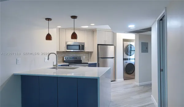 Kitchen featuring an island with a stone-finish countertop, stainless steel appliances, neutral cabinetry, stacked laundry unit, and wood-finish flooring