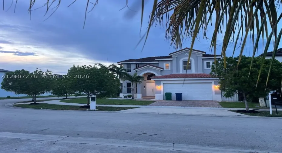 Two-story stucco exterior featuring a tiled roof, multi-gabled facade, arched entryway, and an attached two-car garage with a paved driveway