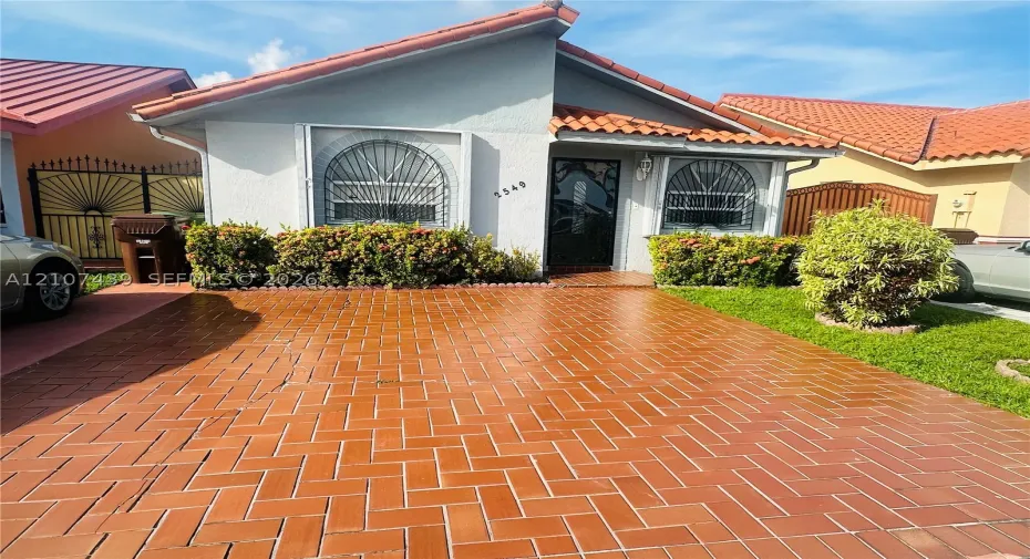 Stucco exterior featuring a red clay tile roof, herringbone-patterned brick paver driveway, and arched window detailing