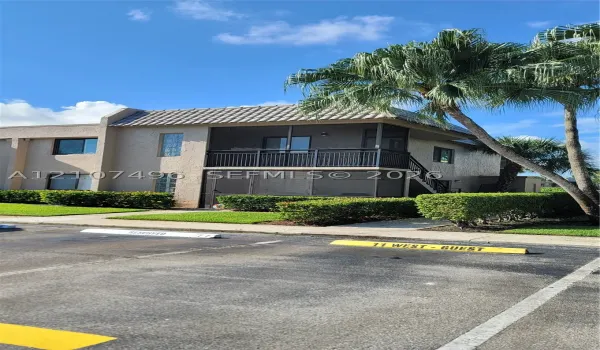 Stucco exterior building featuring a tiled roof, screened-in balcony, and designated guest parking