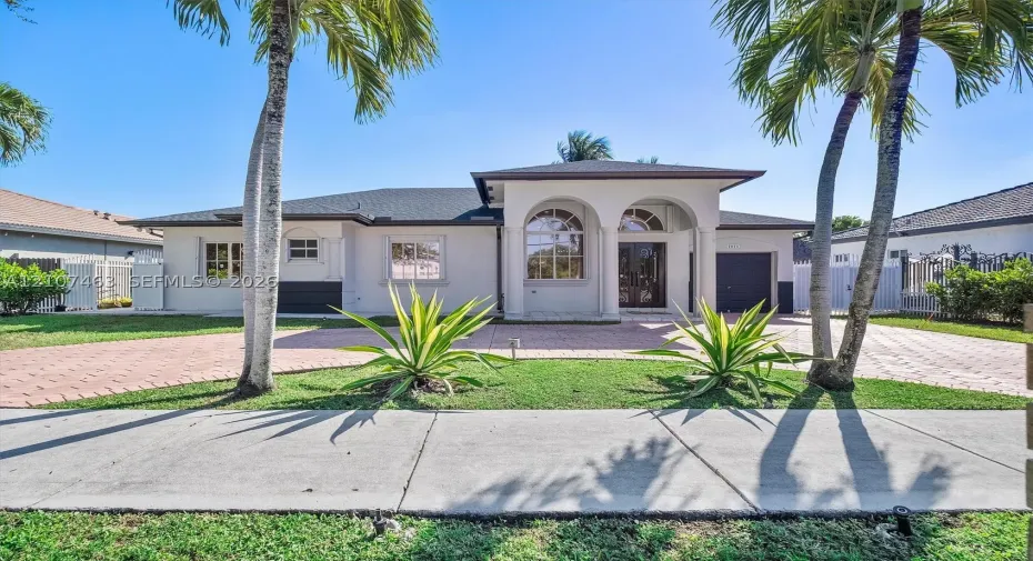 Stucco exterior featuring dual arched entryways, a paved driveway, decorative stone-trimmed windows, and mature palm landscaping