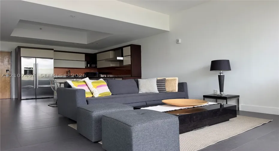 Open-concept area featuring oversized neutral floor tiling, recessed ceiling detail, and kitchen cabinetry with a two-tone finish