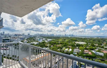 Private balcony with metal railings overlooking an expansive cityscape, waterway, and dense tree canopy