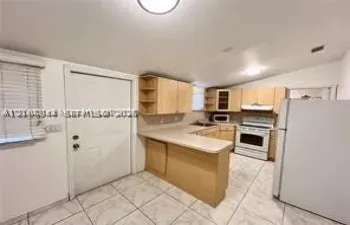 Kitchen featuring light wood-finish cabinetry, a peninsula counter, white appliances, and tiled flooring