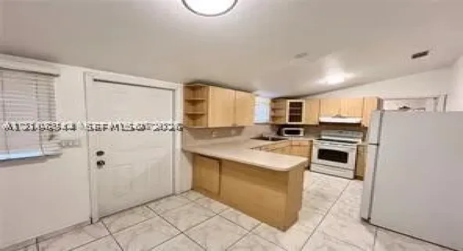 Kitchen featuring light wood-finish cabinetry, a peninsula counter, white appliances, and tiled flooring