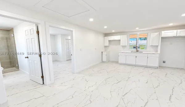 Kitchen featuring white shaker-style cabinetry, stone-patterned tile flooring, recessed ceiling lighting, and a walk-in shower with neutral tile surround