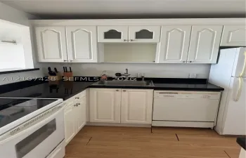Kitchen featuring white cabinetry with glass-panel accents, dark countertops, a stainless steel undermount sink, and wood-finish flooring