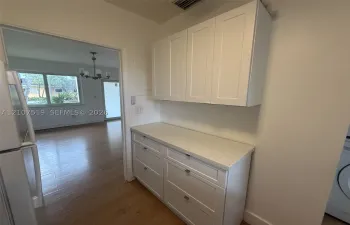 White shaker-style cabinetry with matte hardware, stone-composite countertop, and wood-finish flooring