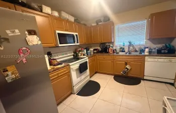 Kitchen featuring wood cabinetry, tile flooring, stainless steel refrigerator, white appliance package, and double basin sink