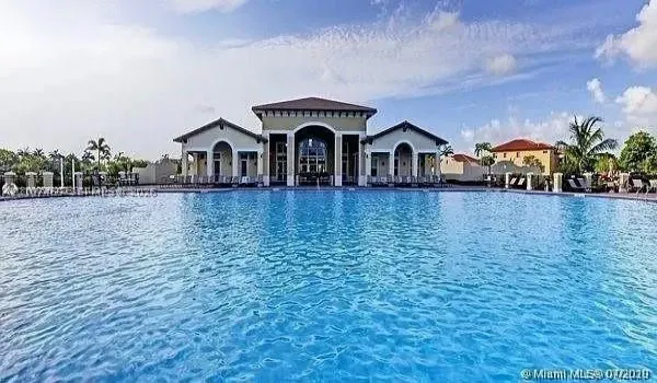 Expansive swimming pool with integrated hardscaping and Mediterranean-inspired clubhouse featuring arched entryways and a multi-gabled roofline
