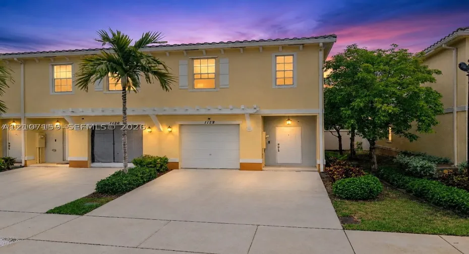 Two-story exterior featuring a tile roof, stucco finish, white-framed windows, a covered pergola accent, and an attached single-car garage with a concrete driveway