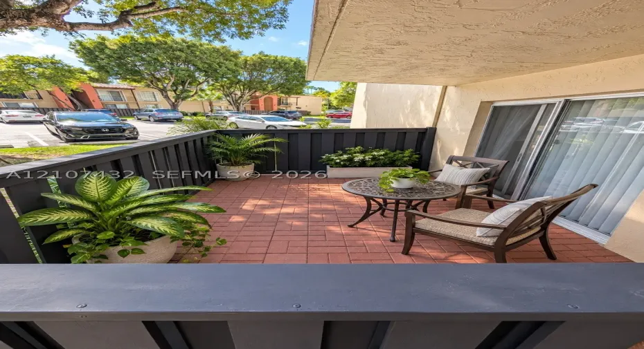 Private balcony featuring terracotta-style paver flooring, dark-painted wood perimeter fencing, and sliding glass entry doors