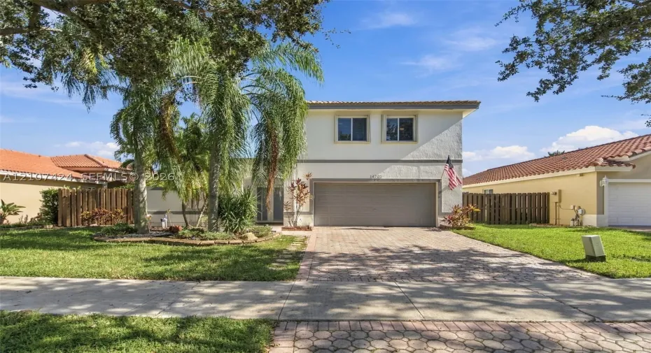 Two-story stucco exterior featuring a multi-car garage, concrete paver driveway, tiled roof, and mature palm landscaping