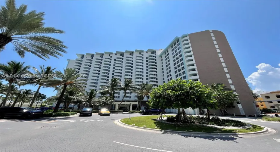 High-rise residential building featuring private balconies, expansive structural facade, and landscaped circular driveway with mature palm trees