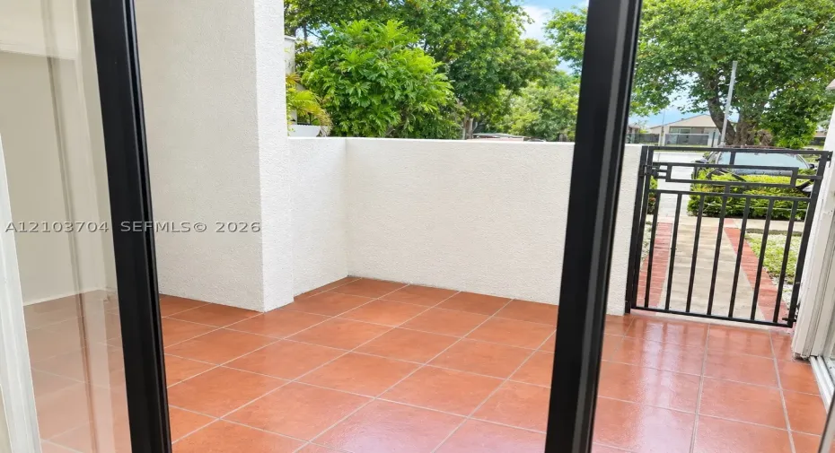 Private outdoor patio featuring terracotta-style tile flooring, high stucco privacy walls, and a secure metal gate entry