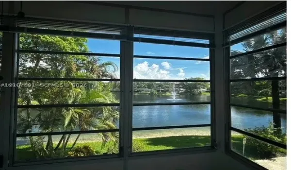 Enclosed space featuring multi-pane horizontal sliding windows, natural scenery with mature palm trees, a pond, and a water fountain