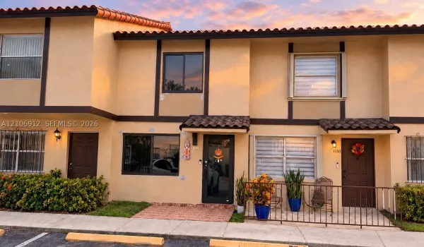 Two-story stucco exterior featuring a tiled roof, dark-framed windows, brick-paved entryway, and metal exterior railings