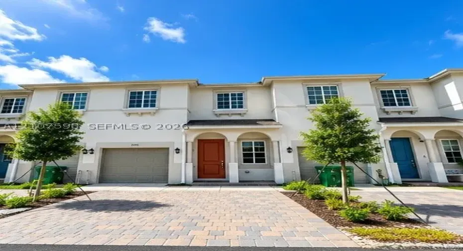 Multi-story exterior featuring light-toned stucco facade, arched entryway detailing, multi-pane windows, and a paved stone driveway with integrated garage access