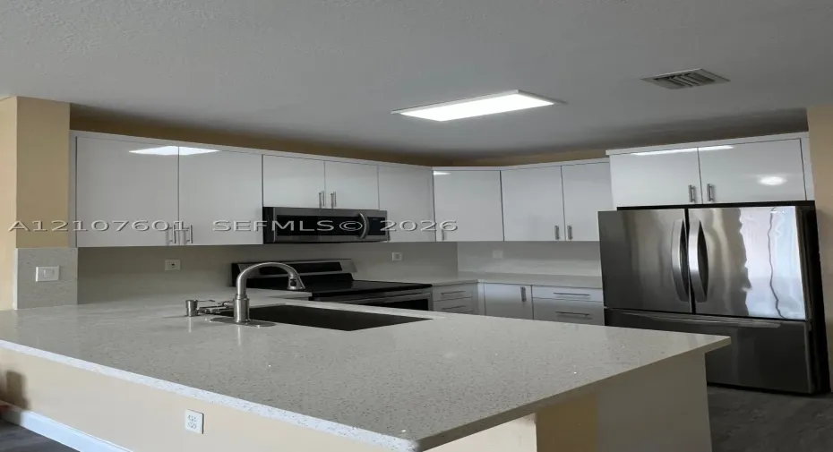 Kitchen featuring white flat-panel cabinetry, quartz countertops, a stainless steel undermount sink with a gooseneck faucet, and stainless steel appliances