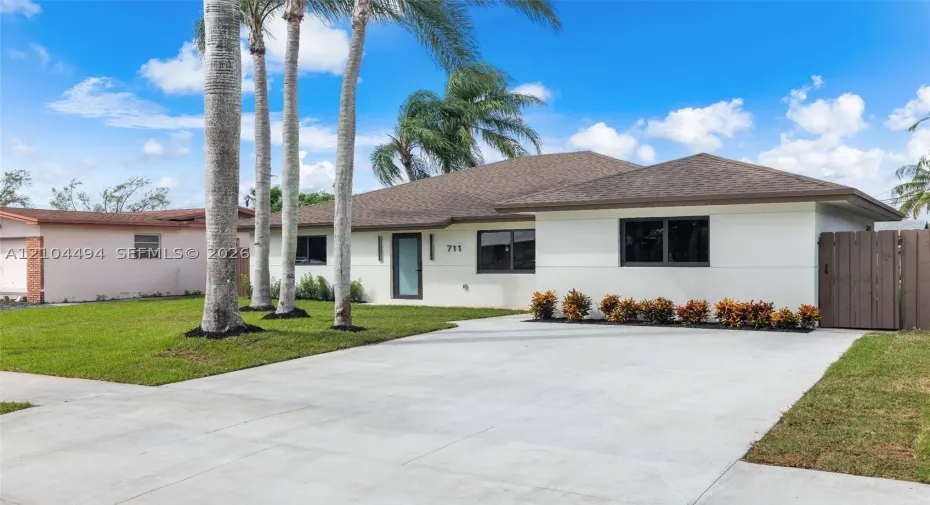 Single-story residence featuring a neutral stucco exterior, a concrete driveway, modern dark-framed windows, and a privacy fence