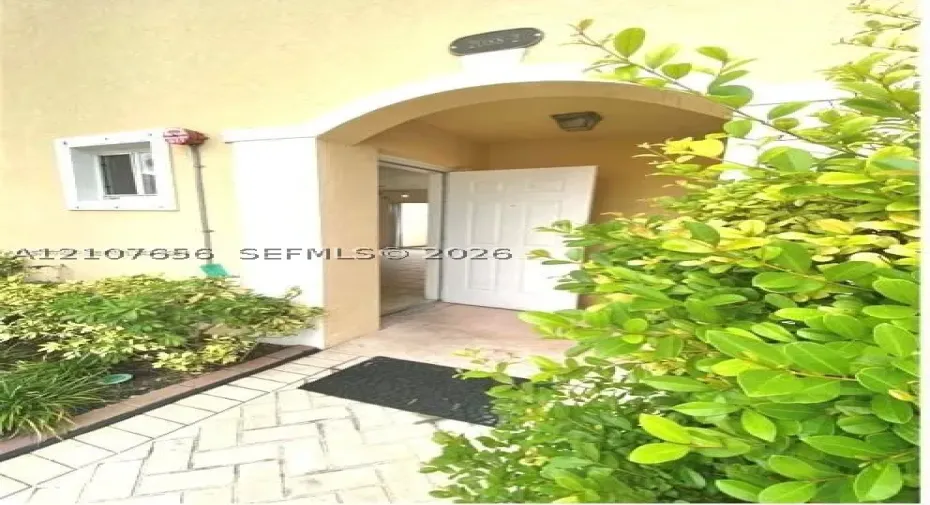 Covered entryway featuring a stucco archway, herringbone-patterned paved walkway, and built-in exterior lighting